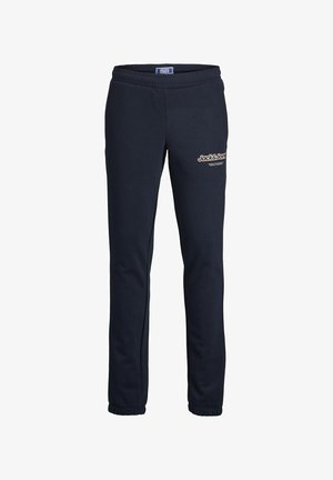 Haut à fermeture éclair bleu marine avec des joggers assortis, présentant un petit logo sur la poitrine et sur le côté. Le matériau est doux et texturé.
