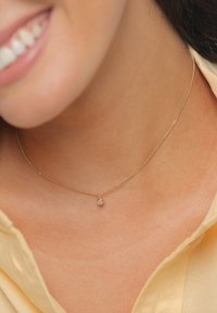 Collar de cadena dorada con un pequeño colgante redondo de piedra preciosa. La cadena es delgada con una textura delicada, situada en la clavícula.