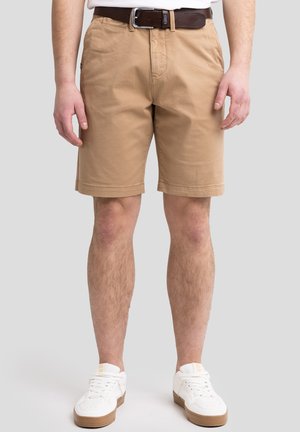 Beige bomuldsshorts med opfoldede kanter, sidelommer og bæltet. Båret med hvide sneakers. Simpel design med en glat overflade.