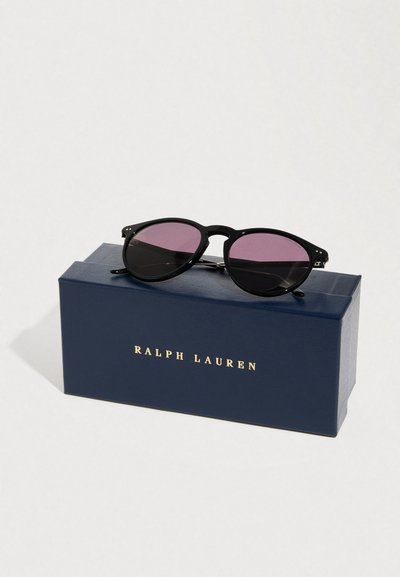 Μαύρα στρογγυλά γυαλιά ηλίου με μοβ φακούς που ακουμπούν σε μια θήκη Ralph Lauren σε σκούρο μπλε χρώμα, πάνω σε λευκό φόντο.