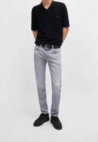 Svart pikétröja med korta ärmar, ljusgrå jeans, svart bälte med silverdetaljer och svarta sneakers. Ledig passform med slät textur.