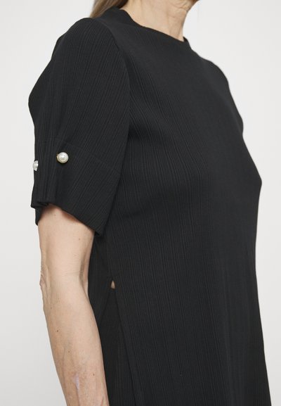 Black ribbed dress featuring short puff sleeves with pearl and gold button accents, side slits, and a round neckline.