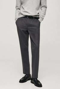Graue Stoffhose mit geradem Schnitt, mit einer dezenten Textur, Gürtelschlaufen und einem schwarzen Gürtel; kombiniert mit schwarzen Slippern.