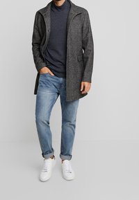 Abrigo gris de mezcla de lana con cuello vuelto, llevado sobre un suéter de cuello alto a rayas marinas, combinado con vaqueros azul claro y zapatillas blancas.