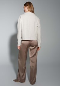Helle beige Pullover mit langen Ärmeln und geradem Schnitt, kombiniert mit hochgeschnittenen, glänzenden taupefarbigen weiten Hosen. Weiche Texturen, minimalistisches Design.
