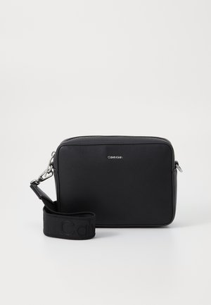 Schwarze rechteckige Tasche aus glattem Leder, mit einem Reißverschluss, glänzenden Beschlägen und einem Stoffgurt mit geprägten Logodetails.