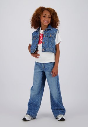 Blå denim cropped vest med knapdetaljer, hvid T-shirt med rød grafik, løse blå jeans med hjerte mønster og hvide sneakers.
