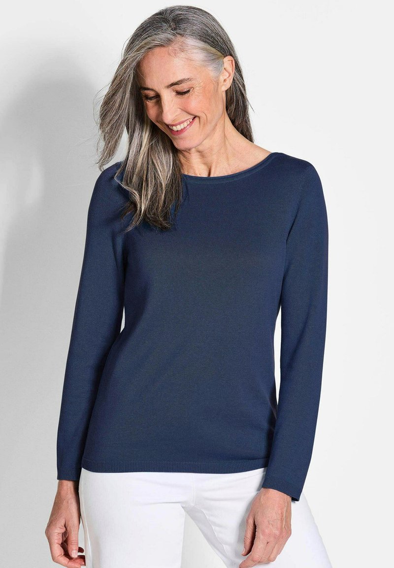 Marineblauer Pullover mit langen Ärmeln und rundem Kragen, mit einem gerippten Muster, getragen mit weißen Hosen. Einfaches und klassisches Design.