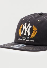 Μαύρο καπέλο μπέιζμπολ των New York Yankees με λευκό λογότυπο, κέντημα από χρυσό δάφνινο στεφάνι και το κείμενο "Yankees American League" στο μπροστινό μέρος.