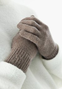 Gants tricotés marron avec des poignets côtelés ; dotés d'un motif texturé et d'un accent décoratif au niveau du poignet, reposant sur un tissu léger.