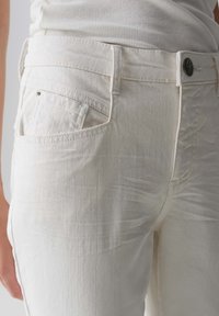 Jeans in denim bianco con un design aderente e una texture liscia. Presentano una tasca posteriore, passanti per la cintura e una chiusura con bottone in metallo.