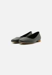 Bailarinas de cuero negro con una textura suave, punta afilada y tacón bajo de madera. Diseño simple sin hardware o acentos visibles.