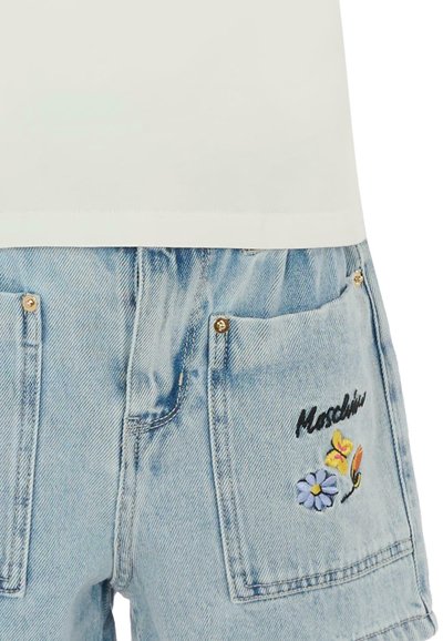 Pantaloni corti in denim azzurro chiaro con tasche frontali, ricamati con una farfalla, un fiore e la parola "Moschino" in carattere corsivo nero.