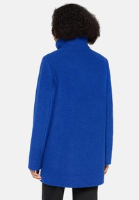 Koninklijk blauwe wollen jas met een hoge kraag en lange, recht gesneden mouwen. De textuur is glad, met een nette afwerking en geen zichtbare hardware.