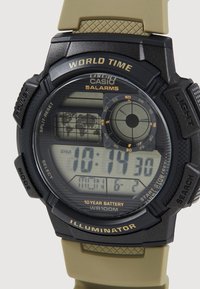 Montre numérique Casio avec un boîtier en résine noire, un bracelet en silicone vert, plusieurs affichages et des fonctions pour l'heure mondiale, l'alarme et l'illumination.