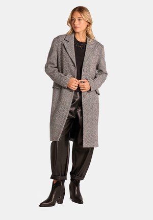Abrigo gris de espiga con cuello, mangas largas y abertura frontal, combinado con pantalones de satén negros y botines que presentan acentos texturizados.