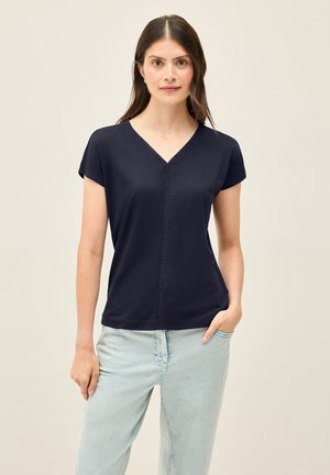 T-shirt bleu marine à manches courtes et col en V, présentant un panneau avant texturé et une coupe décontractée, associé à un jean bleu clair.