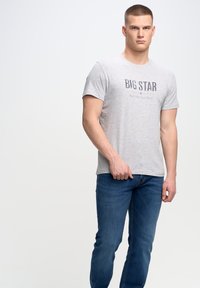 Pilkas trumpa rankovė t-shirt su tamsiai mėlynu užrašu "BIG STAR". Dėvimas su tamsiai mėlynomis džinsinėmis kelnėmis. Lygi tekstūra, kasdienis modeliukas.