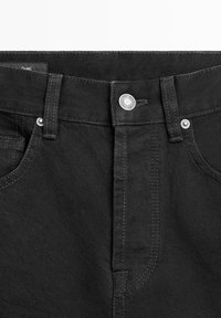 Schwarze Denim-Jeansbund mit Knopf, Gürtelschlaufen, Nieten und teilweise sichtbaren Taschen auf weißem Hintergrund.