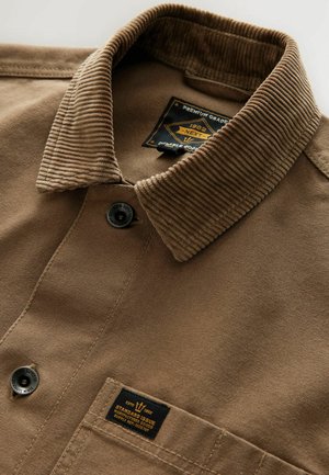 Barna ing, corduroy gallérral, gombos záródással, szövet címkével és textúrált felülettel. Fő részlet egy kis folt a szegély közelében.