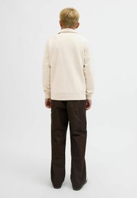 Ljusbeige sweatshirt med krage, avslappnad passform, ribbade ärmslut och slät textur. Kombineras med mörkbruna vida byxor.