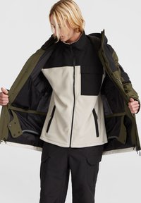 Mørkegrøn og sort jakke med en cremefarvet fleece-inderside, lynlåslommer og en frontlomme, med et robust, lagdelt design.