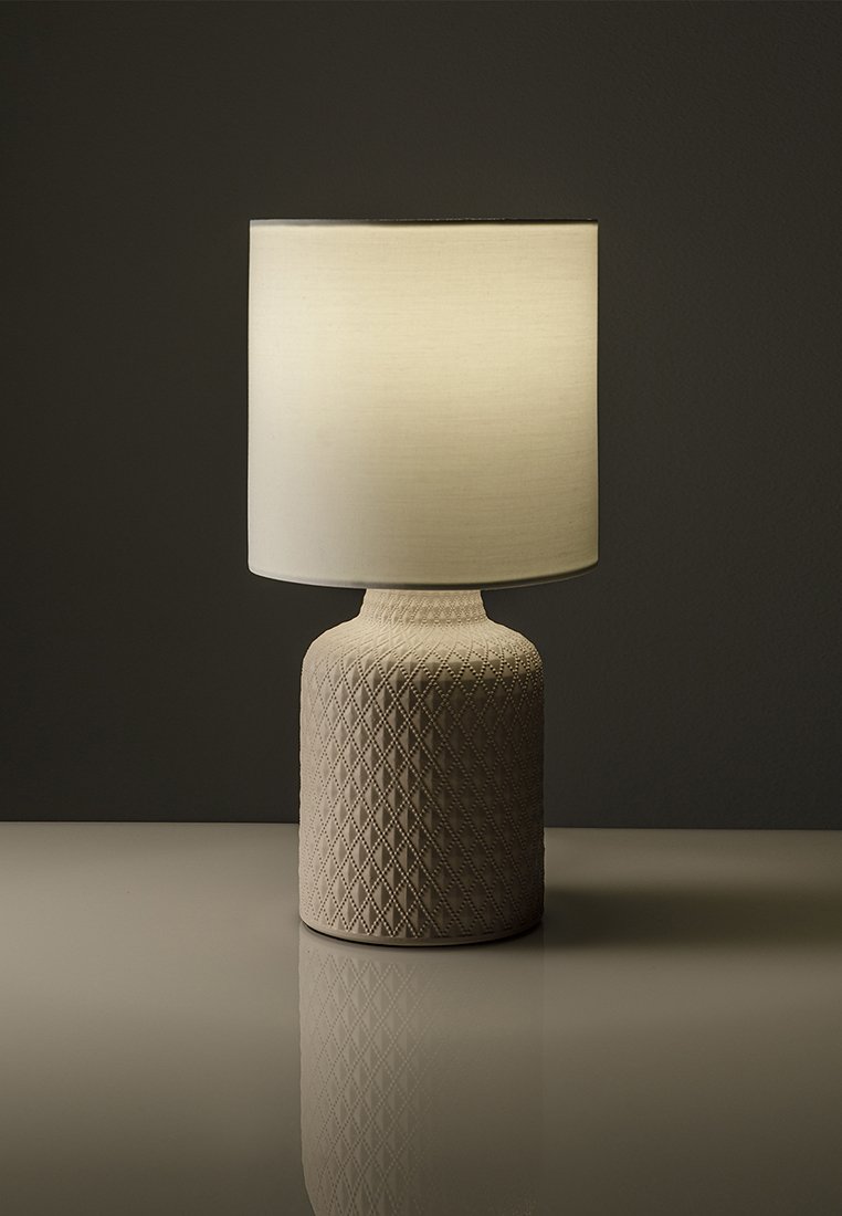 Tischlampe mit einem strukturierten beigen Keramikfuß, der ein Diamantmuster aufweist, und einem zylindrischen weißen Stoffschirm, der sanftes Licht ausstrahlt.