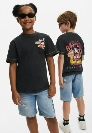 Sort grafisk T-shirt med gul syning, prydet med Mickey Mouse tryk. Sammen med slidte denim shorts og hvide sneakers.