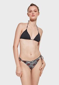 Top de bikini negro con copas triangulares y lazos a rayas, acompañado de un fondo con patrón de cebra que presenta acentos rojos y lazos ajustables en los laterales.
