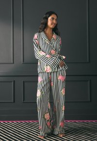 Pajama set s crno-bijelim prugama i ružičastim cvjetnim uzorkom. Gornji dio ima šal zaključak, a hlače su široke i ležerne.