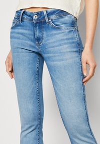 Ljusblå jeans i denim, med smal passform, urtvättad textur, femfickdesign och en silverfärgad knapp i midjan.