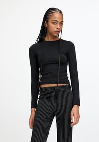 Top negru cu mânecă lungă și decolteu rotund, realizat dintr-un material neted, asortat cu pantaloni cu dungi fine negre și albe, având un design ajustat.