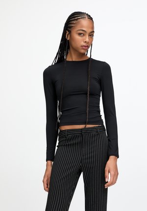 Black long-sleeve top with a round neckline, made of smooth fabric, paired with black and white pinstripe trousers, featuring a fitted design.