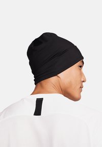 Berretto nero realizzato in tessuto elastico e liscio, caratterizzato da una vestibilità aderente e cuciture minime, indossato con una maglietta atletica bianca.