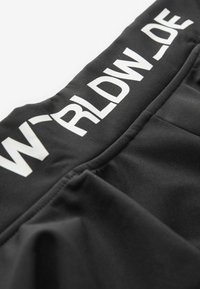 Gros plan sur un tissu noir avec texte blanc imprimé "WRLDW_DE" sur une ceinture ou une couture d'ourlet.
