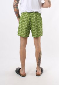 Pantaloni corti verdi con un motivo ripetuto di testo in nero "Emporio Armani". Vita elasticizzata e vestibilità comoda. Abbinati a calzature casual nere.