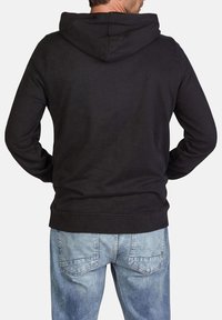 Sudadera negra con capucha, de acabado texturizado, que cuenta con capucha ajustable, mangas largas y puños acanalados, combinada con jeans de color azul claro.