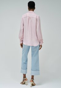 Camisa de manga larga rosa claro con una textura sutil, puños abotonados y tela suave, combinada con jeans de pierna ancha azul claro y tacones con tiras.