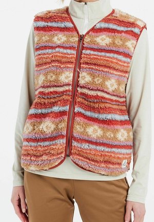 Pluizig vest met rits en horizontale strepen in rood, oranje, beige, blauw en roze, gedragen over een crème top met lange mouwen en een broek in het bruin.