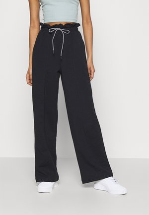 Person wearing black wide-leg pants with a drawstring waist, light blue cropped top, and white sneakers, standing against a plain background.