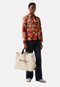 Kurtka w kwiatowy wzór w wielokolorowej tonacji z czerwonymi i zielonymi odcieniami; niebieskie dżinsy; beżowa torba na ramię z płótna z czarnymi uchwytami i logo.