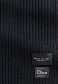 Marineblauw geribbelde kasjmierstof met twee zwarte labels: het merklabel Marc O'Polo en een onderhoudsetiket dat aangeeft dat het voor 100% uit kasjmier bestaat.