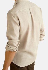 Chemise en lin beige avec col, manches retroussées et un pli central dans le dos, présentant une texture lisse et une coupe décontractée.