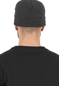 Grå strikket beanie med en kant, med en sømløs top og tekstureret mønster. Båret med en sort t-shirt. Vist fra bageste synsvinkel.