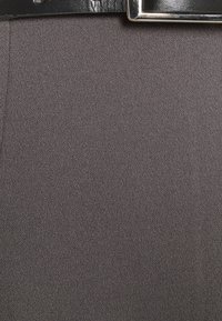 Šedá tkanina s texturovaným povrchem, zdobená černým koženým páskem se stříbrnou obdélníkovou sponou v pase.