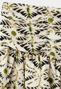 Tissu blanc à texture froncée présentant un motif floral de pétales noirs et beiges avec des centres et des tiges verts.