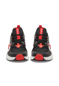 Melnas sporta kurpes ar sarkaniem akcentiem, tīkla augšdaļa un balta zole. Ievērojama šņorēšanas dizains un izteikta zīmola identifikācija uz mēles.