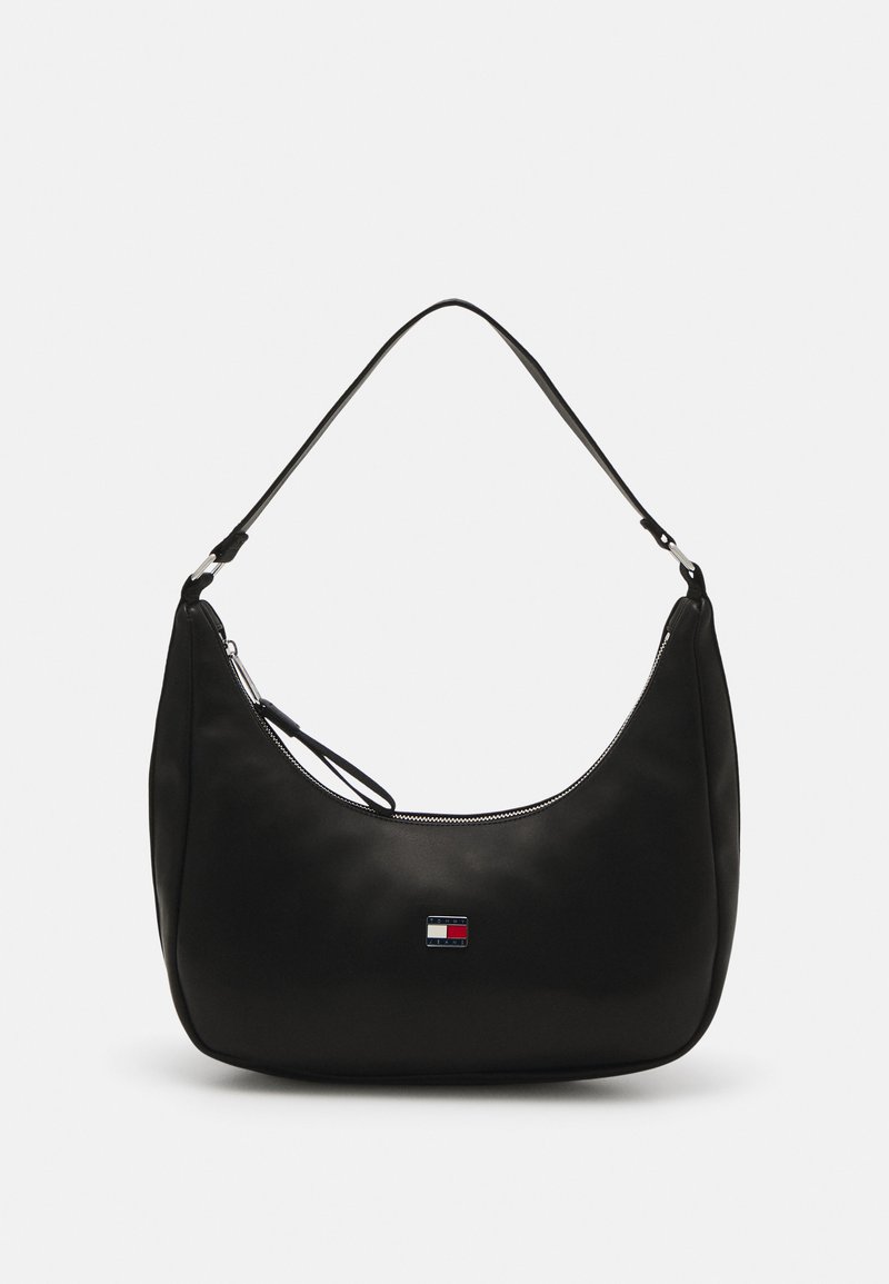 Bolso de hombro negro de nailon con forma curvada, cremallera plateada y un pequeño parche con logo en colores rojo, blanco y azul. Textura suave.