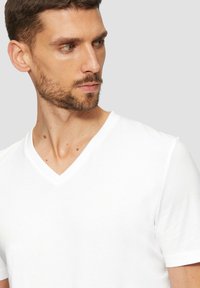 Biela bavlnená tričko s výstrihom do V a krátkymi rukávmi. Hladká textúra, minimálne značkovanie a voľný strih.