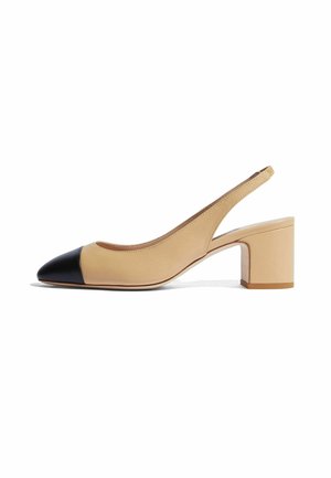 Zapato slingback de cuero beige con punta negra en forma de flecha. Presenta un tacón cuadrado grueso y una textura suave, con detalles de costura mínimos.